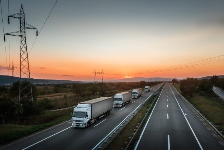 Four White Lorry Trucks Convoy on highway at beautiful sunset